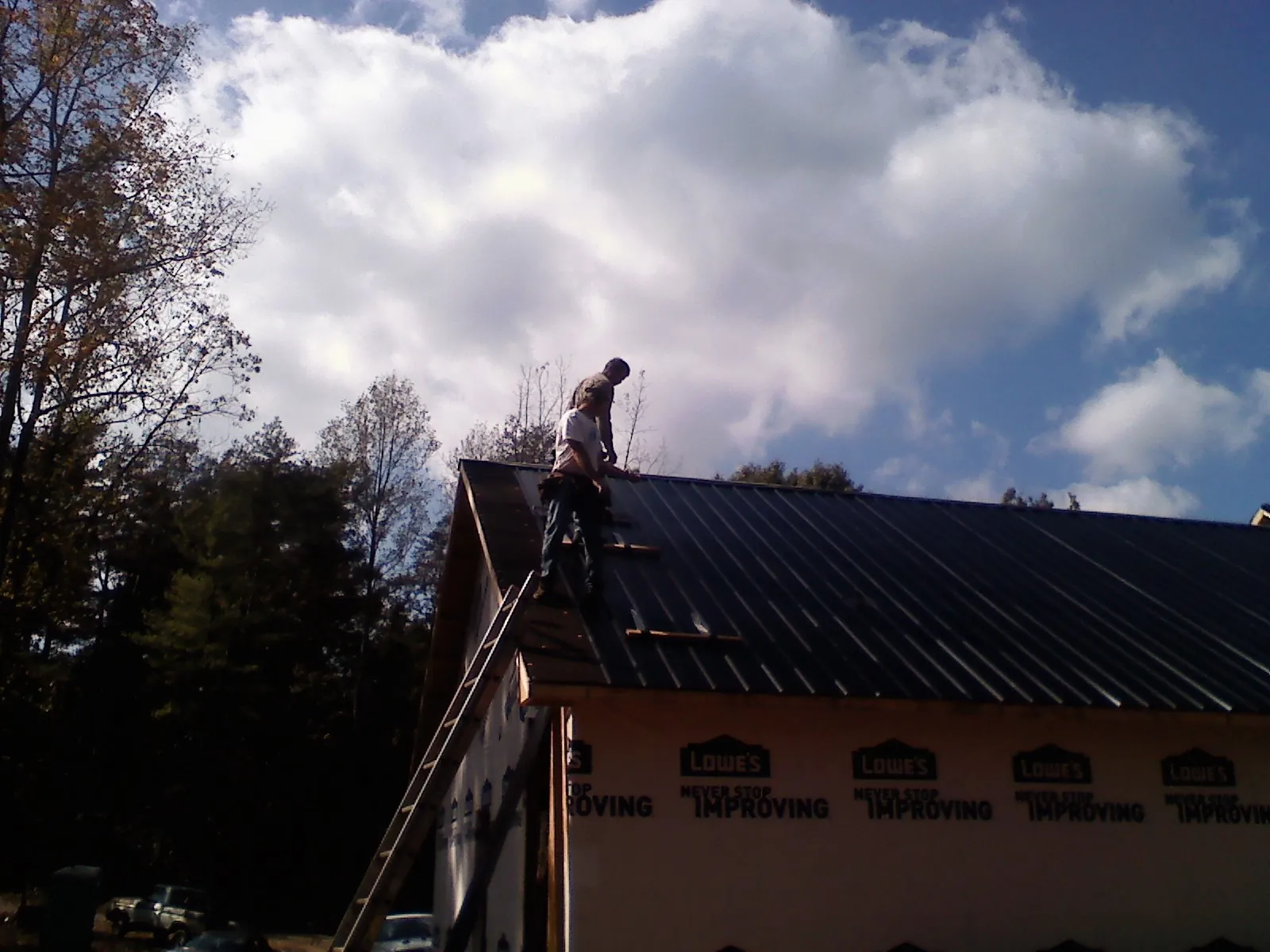 Roofer fastening dark metal panels high against a cloudy sky, from a Roof Inspection job in Clinton